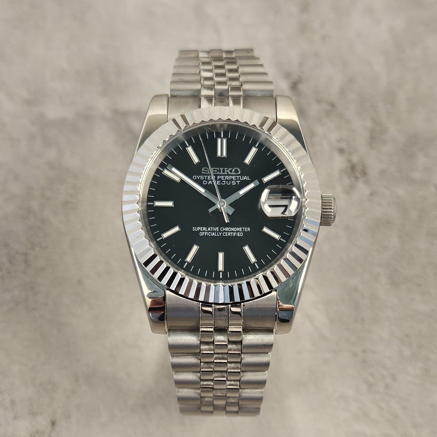 Silver Seiko watch with black dial on a gray textured background