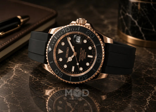Black and rose gold watch on a reflective surface with a pen and notebook in the background