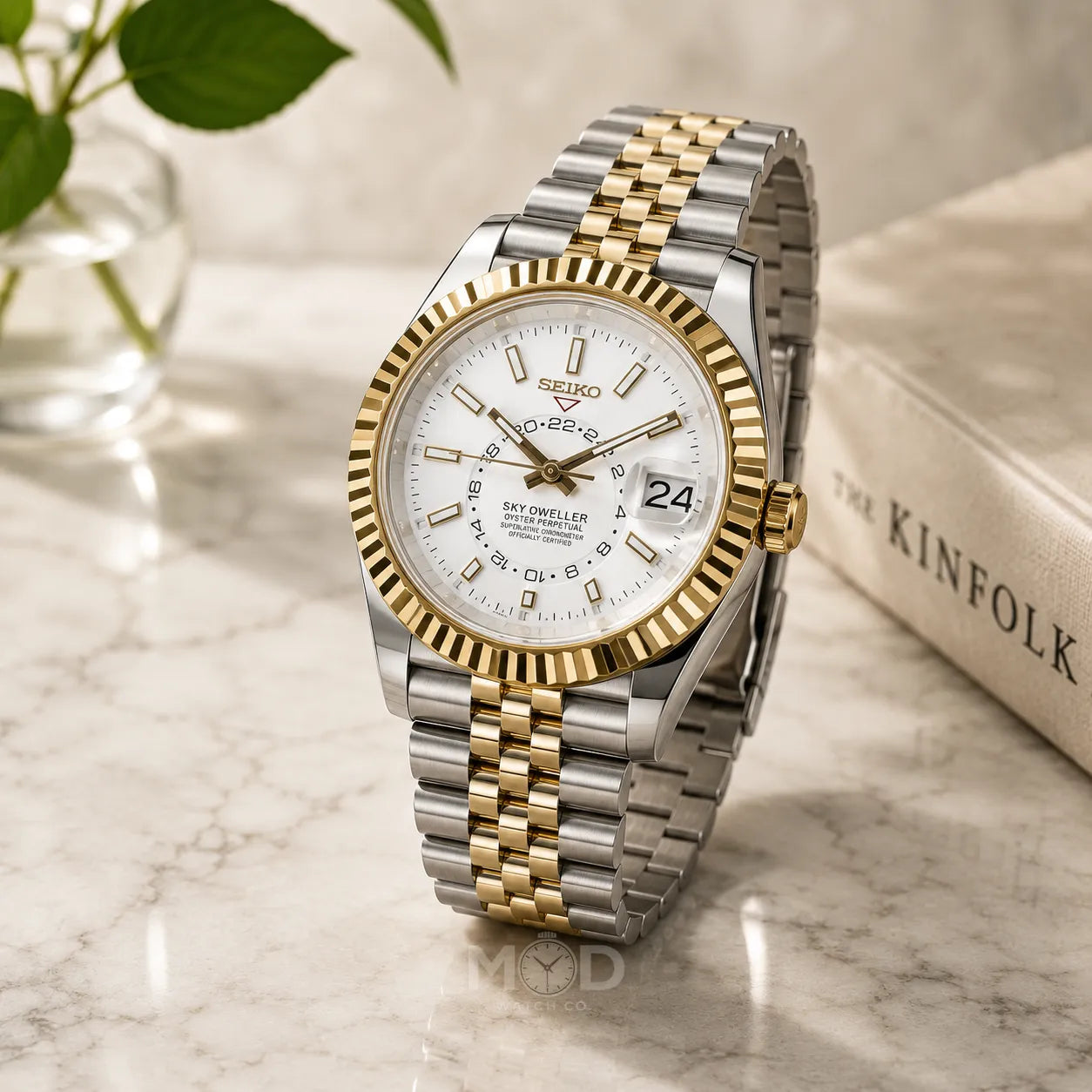 Two-tone Seiko watch on a marble surface with a blurred book and plant in the background