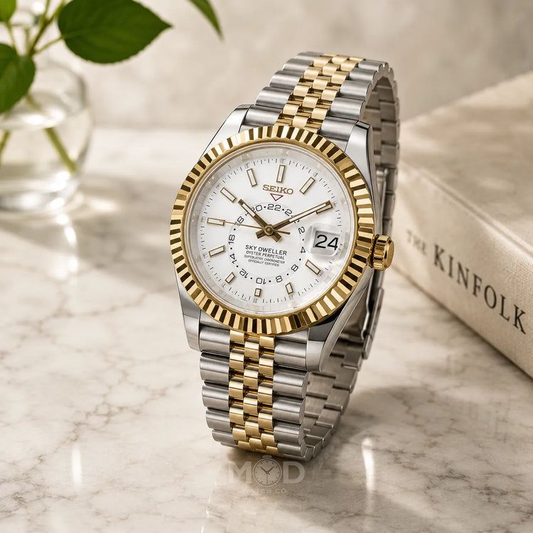 Two-tone Seiko watch on a marble surface with a blurred book and plant in the background