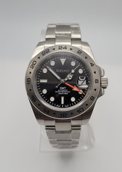 Seiko watch with black dial and silver metal strap on a light gray background