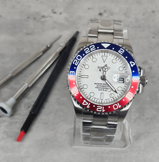 Marine Master watch with red and blue bezel on a gray surface with tools.