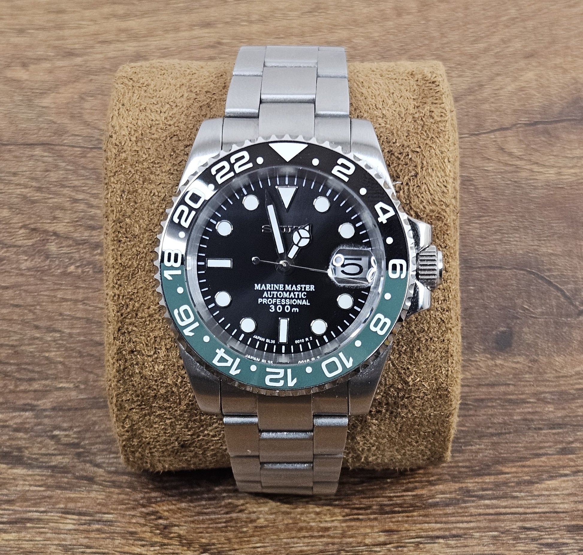 Silver watch with black dial on a brown cushion against a wooden background