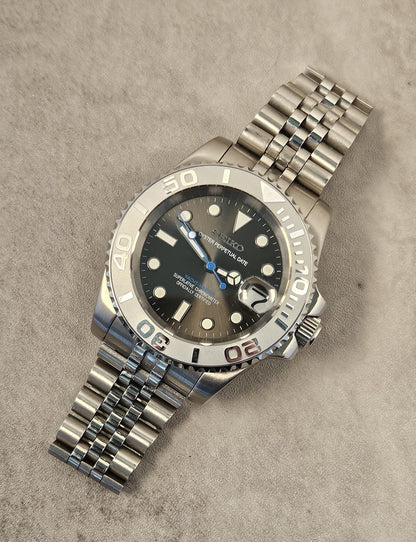 A luxurious silver-toned watch with a grey sunburst dial, luminous hands, a unidirectional rotating bezel, and a stainless steel bracelet on a textured background.