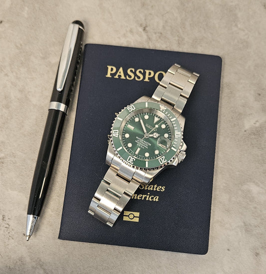 A custom mod Seiko watch with a green dial and green ceramic bezel, a silver stainless steel bracelet, displayed on top of a passport with a pen next to it.