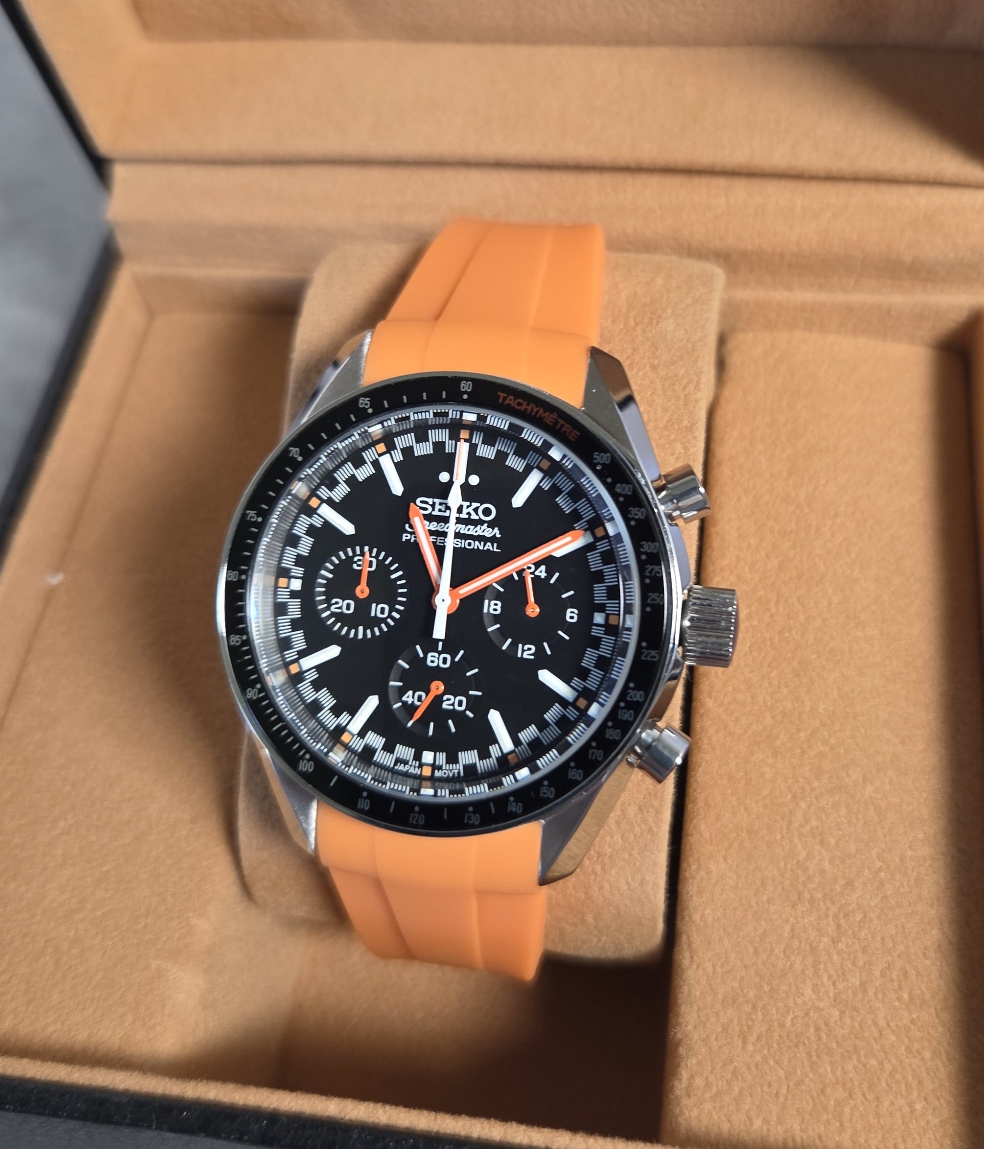 Wristwatch with orange strap on a brown cushioned surface