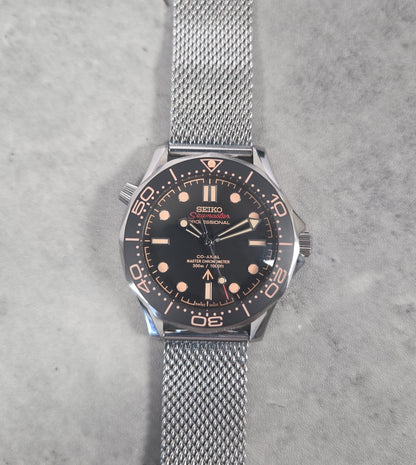 Seiko watch with black dial and silver mesh band on a gray background