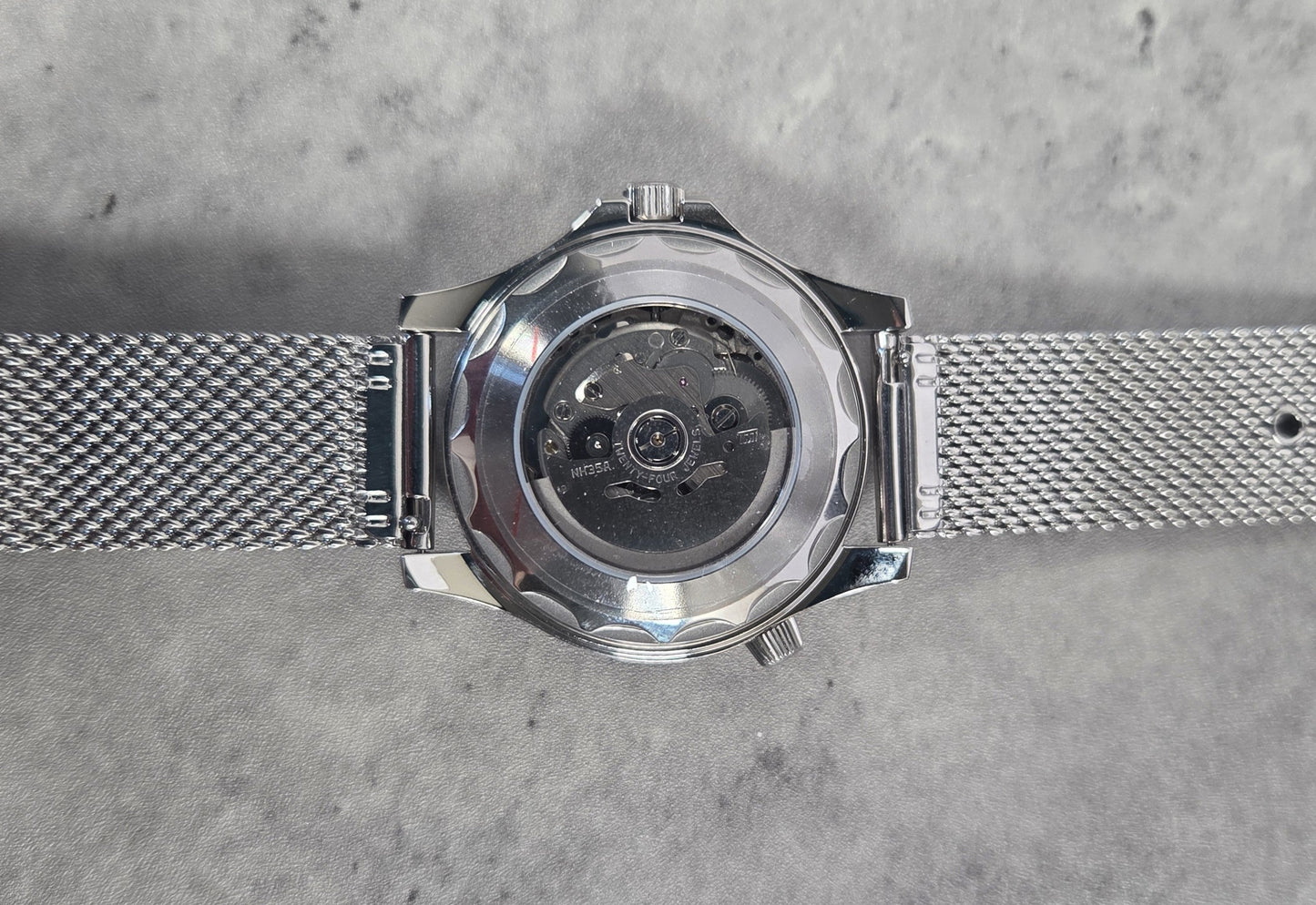 Silver watch with mesh band on a gray textured background