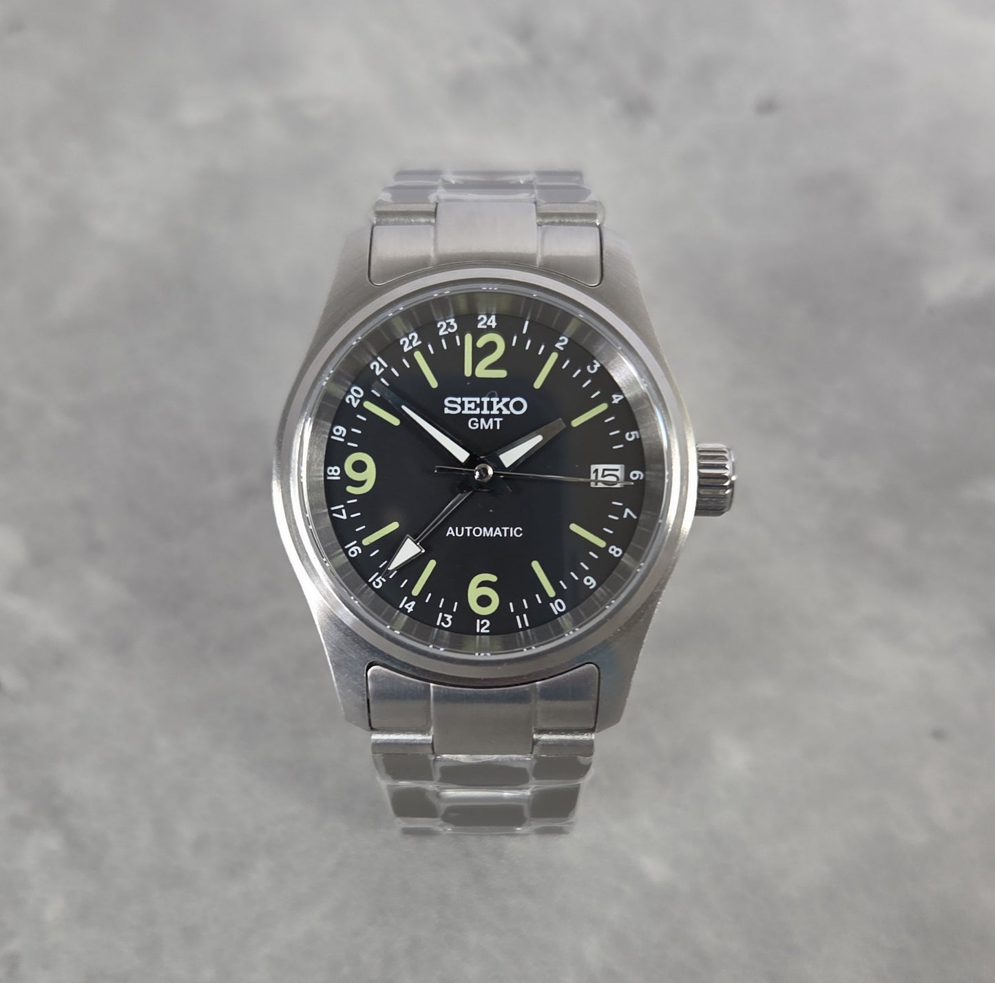 Seiko watch with black dial and silver metal strap on a gray background
