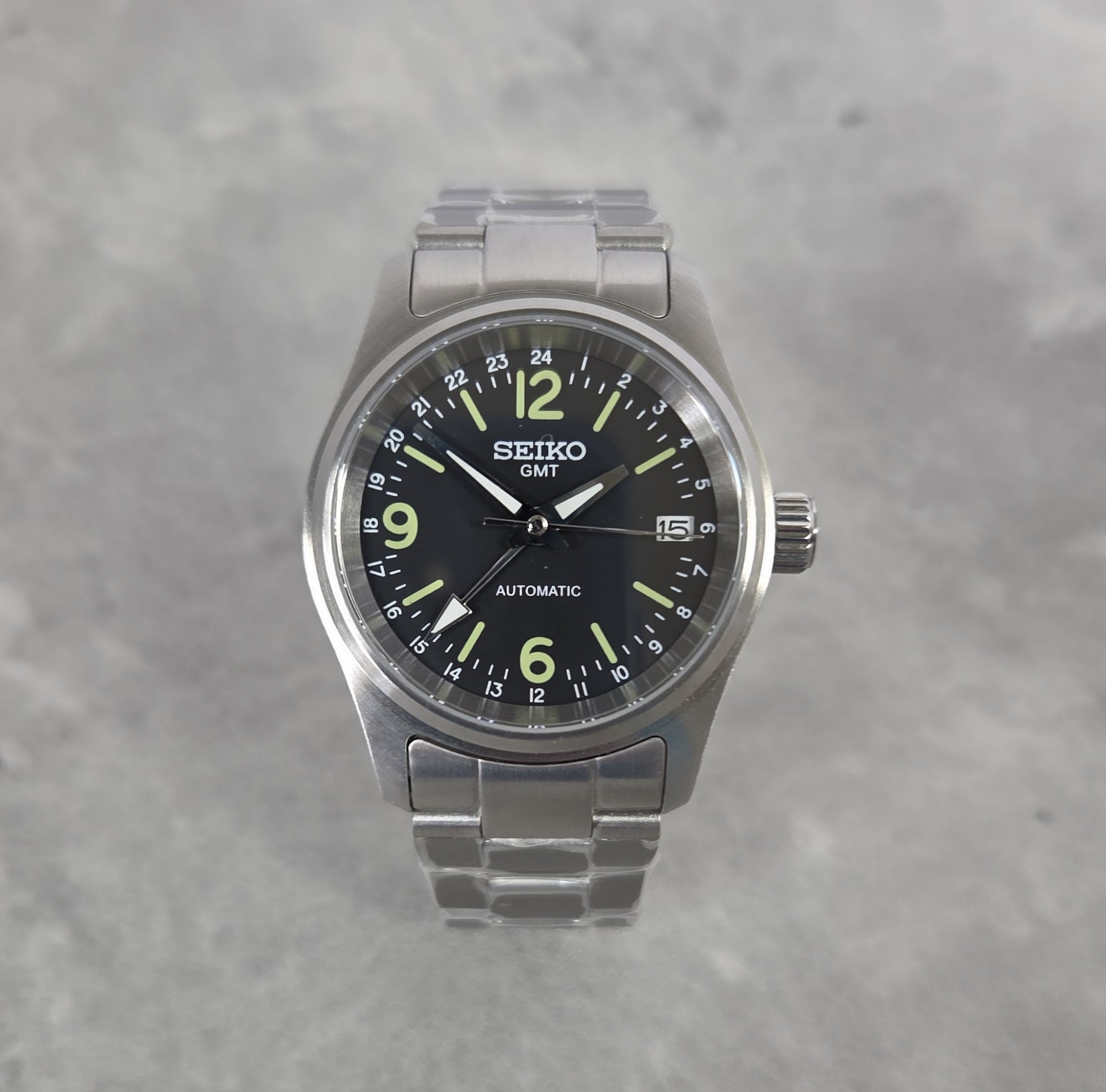 Seiko watch with black dial and silver metal strap on a gray background