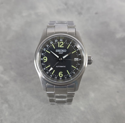Seiko watch with black dial and silver metal strap on a gray background