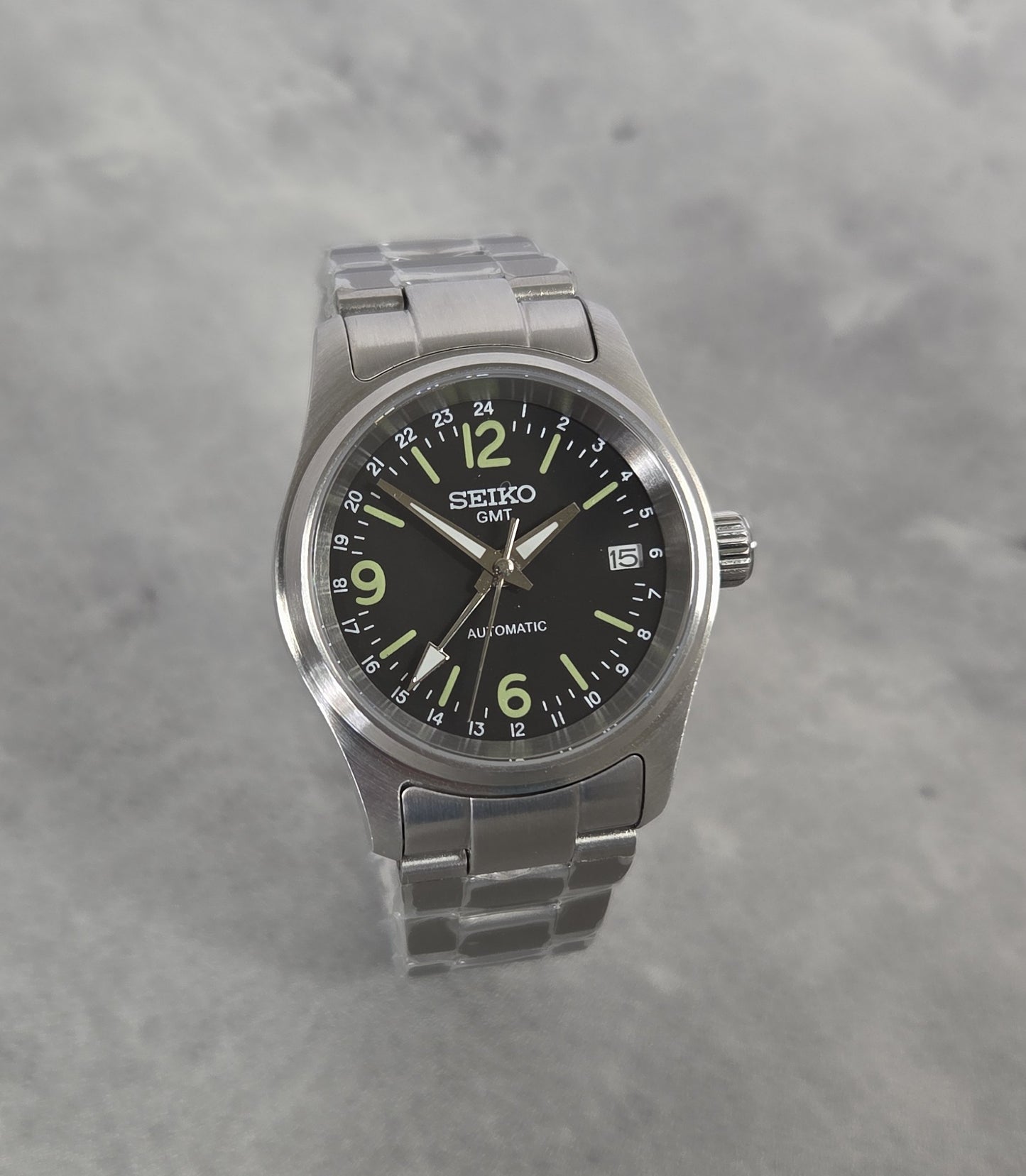 Seiko watch with black dial and silver metal strap on a gray background
