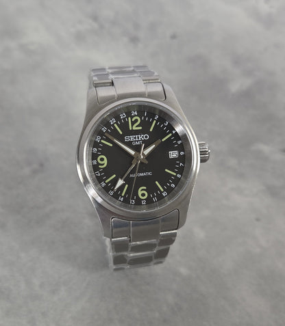 Seiko watch with black dial and silver metal strap on a gray background