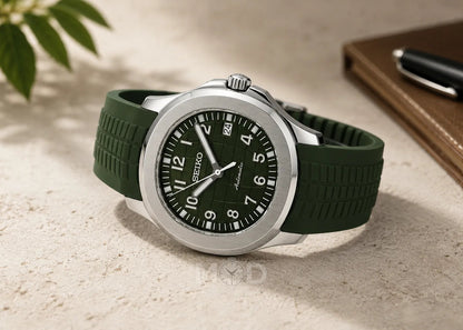 Green wristwatch with a black dial on a light surface, next to a pen and notebook.