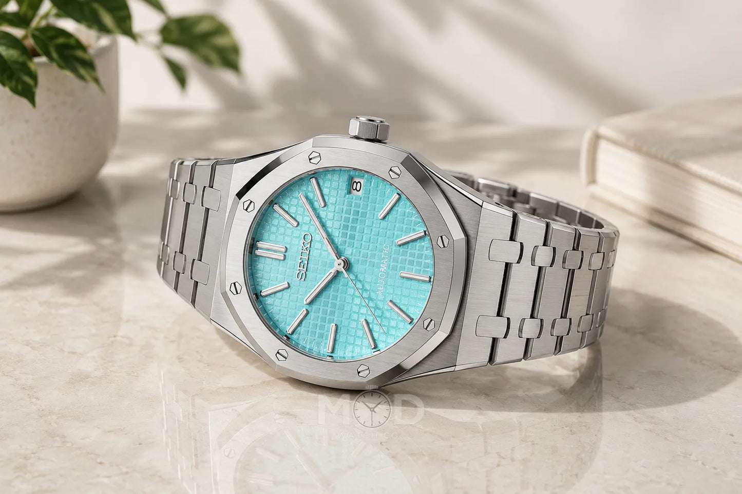 Silver watch with turquoise dial on a light surface
