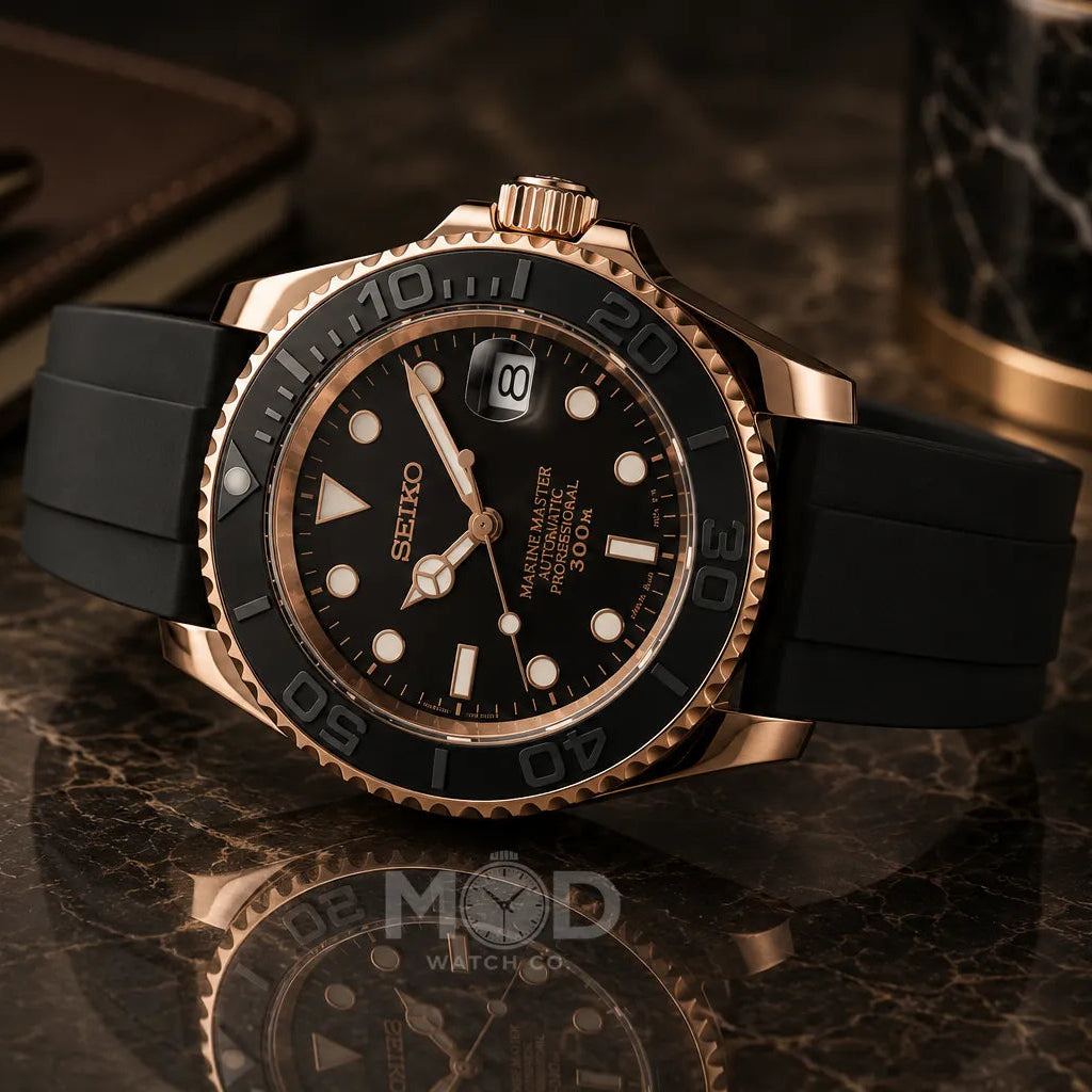Black and rose gold watch on a reflective surface with a pen and notebook in the background