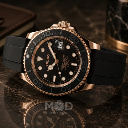 Black and rose gold watch on a reflective surface with a pen and notebook in the background
