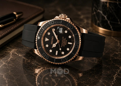 Black and rose gold watch on a reflective surface with a pen and notebook in the background