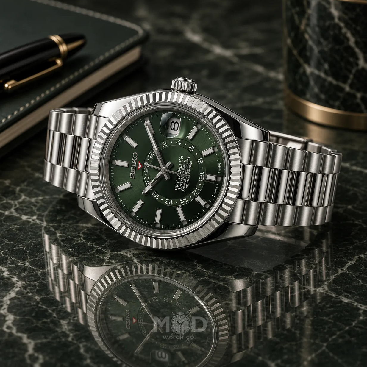 Silver watch with green dial on a reflective surface