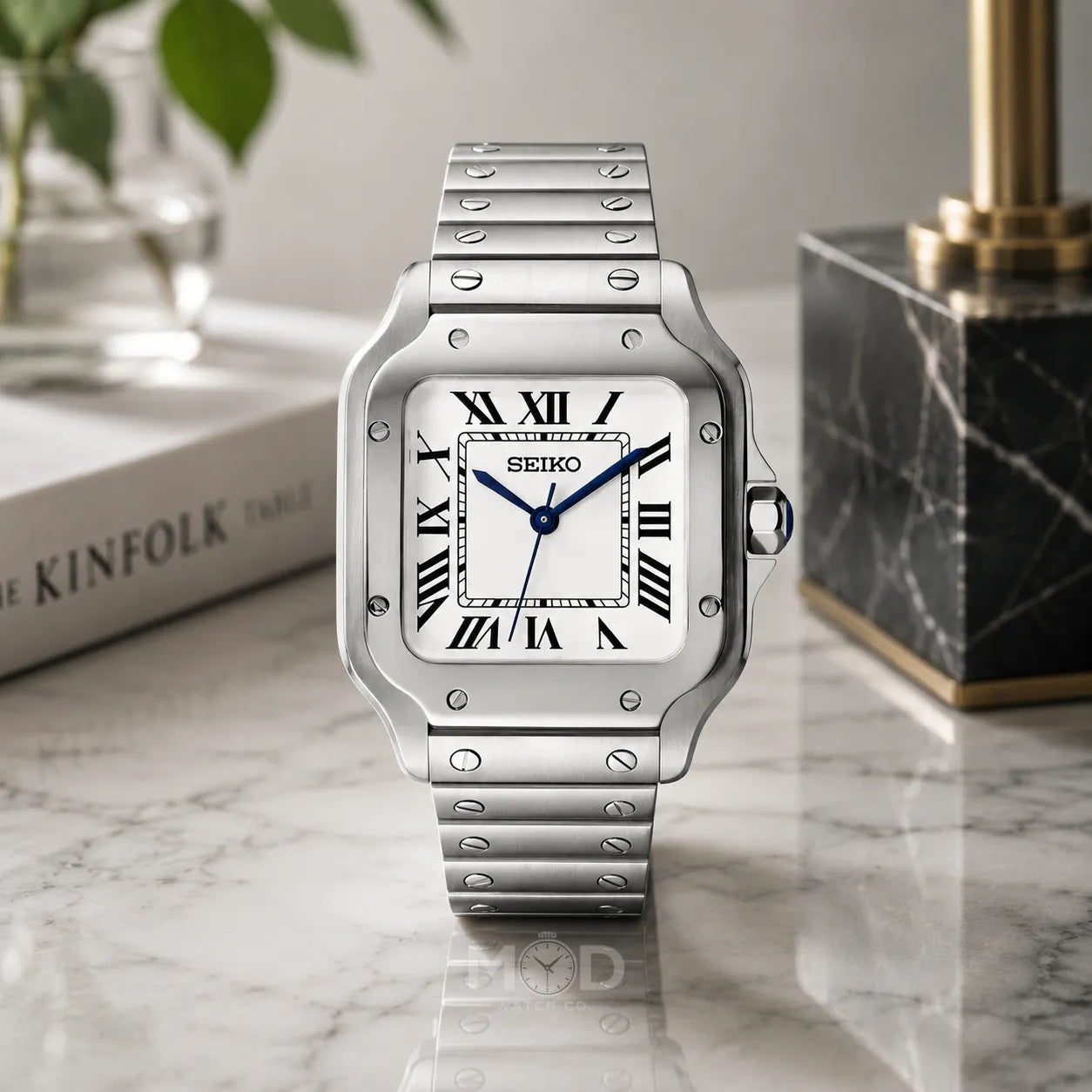 Silver Seiko watch on a marble surface with a book and decorative item in the background