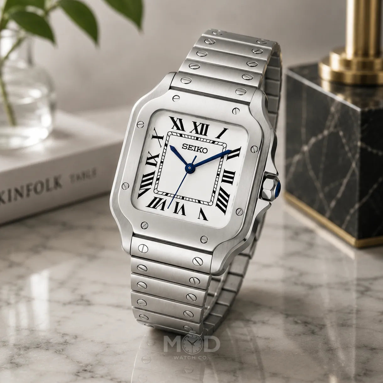 Silver Seiko watch on a marble surface with a plant and book in the background