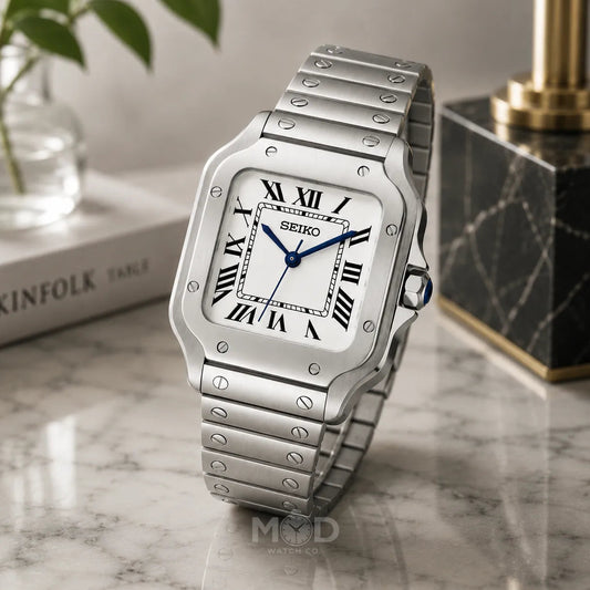 Silver Seiko watch on a marble surface with a plant and book in the background