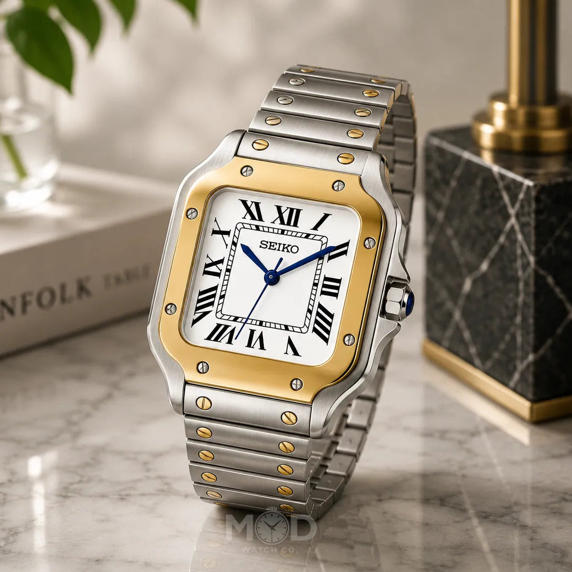 Silver and gold Seiko watch on a marble surface with a blurred background