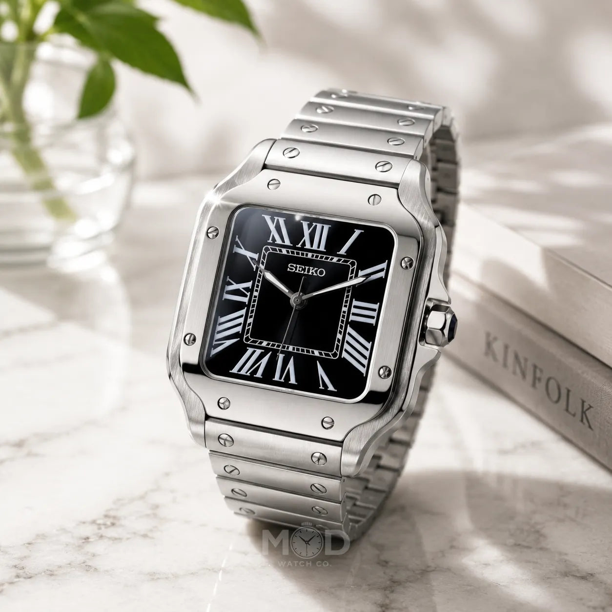 Silver Seiko watch with black face on a marble surface with a plant in the background