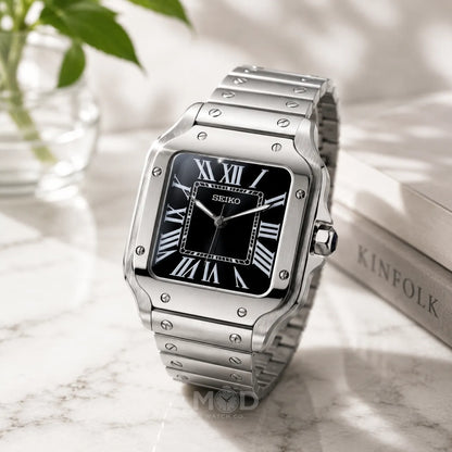 Silver Seiko watch with black face on a marble surface with a plant in the background
