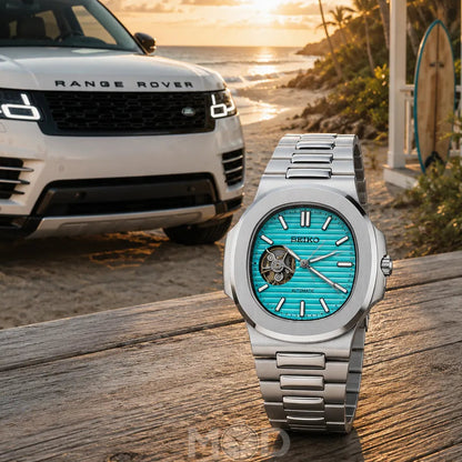 Silver watch with turquoise face on a wooden surface, Range Rover in the background.
