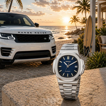 Silver watch with blue face on a stone surface, Range Rover in the background at sunset.