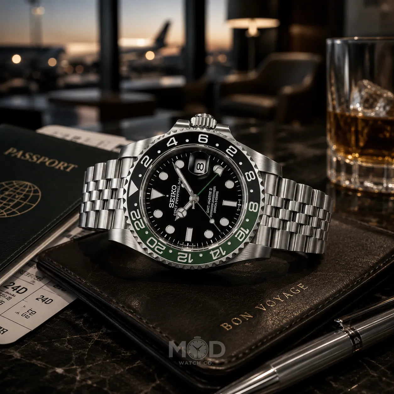 Silver watch with black and green face on a travel-themed surface with passport and tickets.