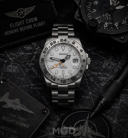 Silver Seiko watch on a dark background with aviation-themed decor