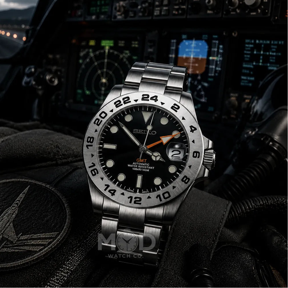 Silver watch with black face on a pilot's dashboard with instruments and helmet in the background