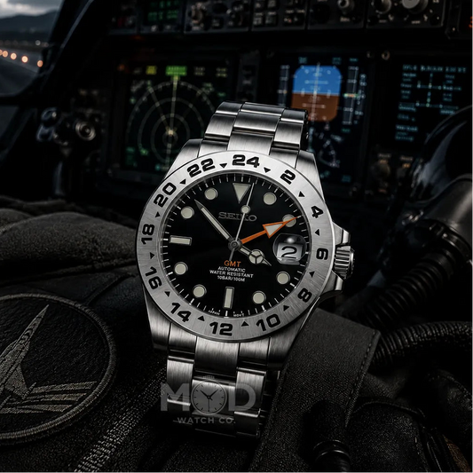 Silver watch with black face on a pilot's dashboard with instruments and helmet in the background