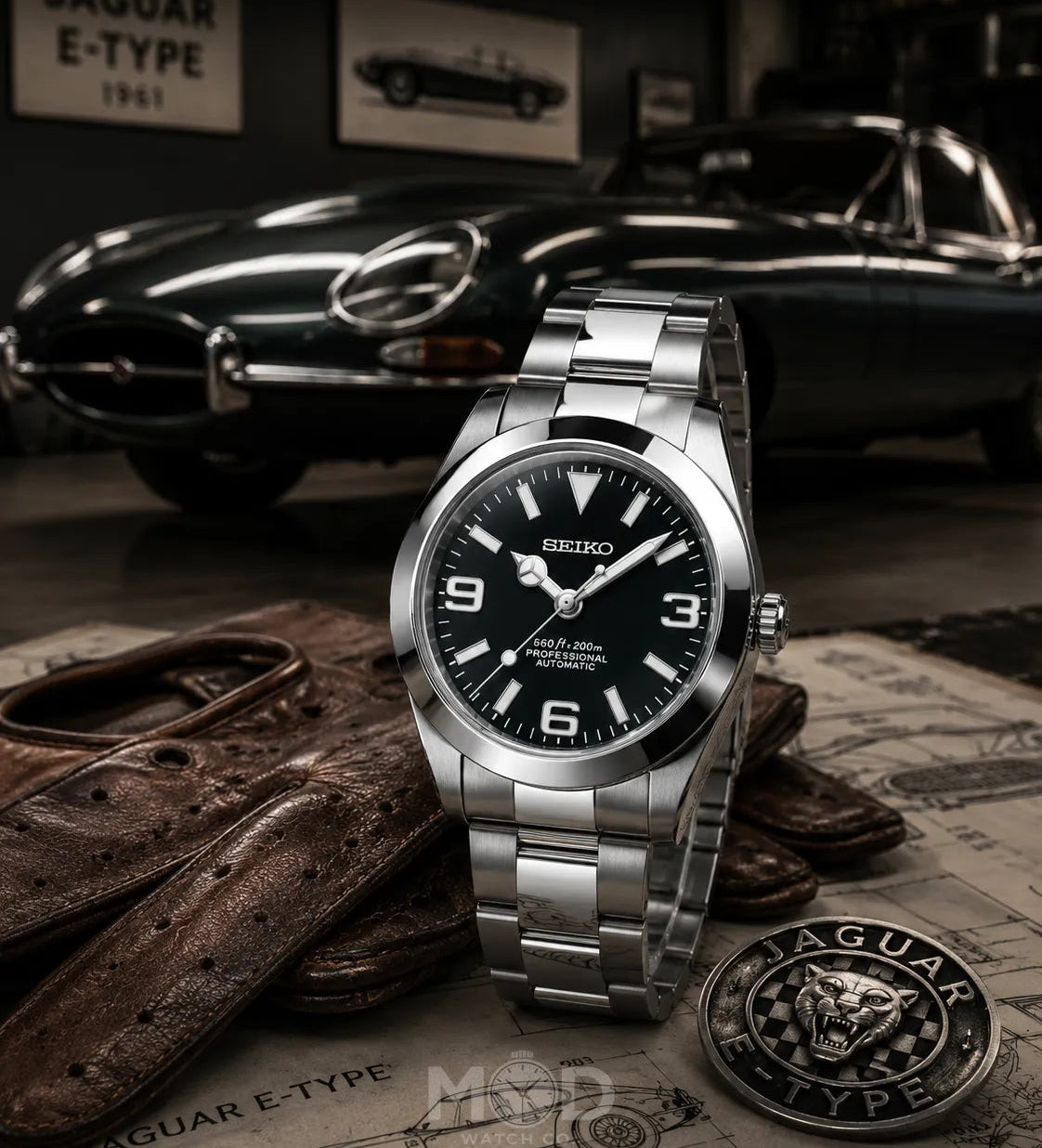 Silver Seiko watch with black dial on a surface with Jaguar E-Type car in the background