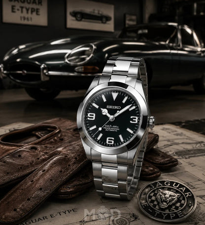 Silver Seiko watch with black dial on a surface with Jaguar E-Type car in the background