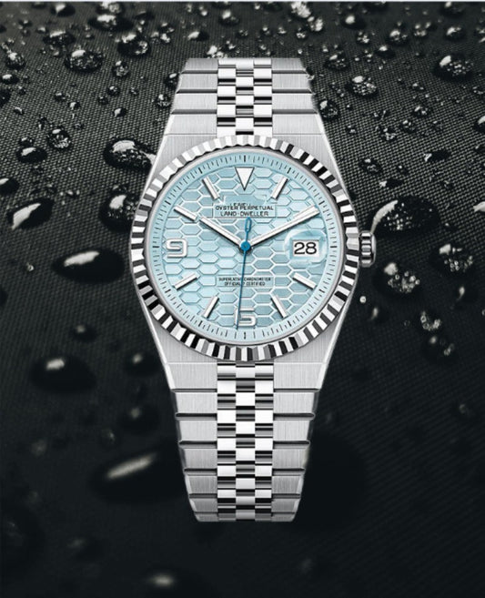Silver Seiko watch with a blue textured face on a black background with water droplets.