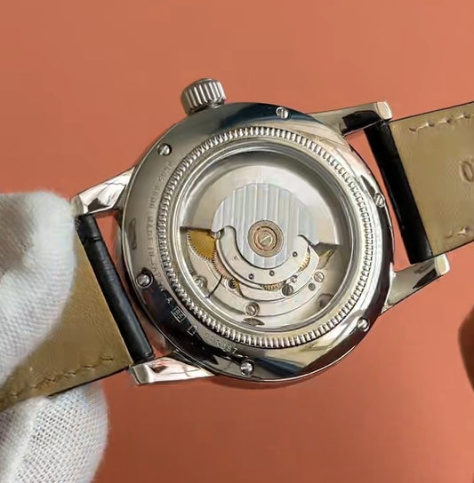 Close-up of the back of a wristwatch with a transparent case showing the automatic mechanical movement, held by a white glove against a solid peach background.