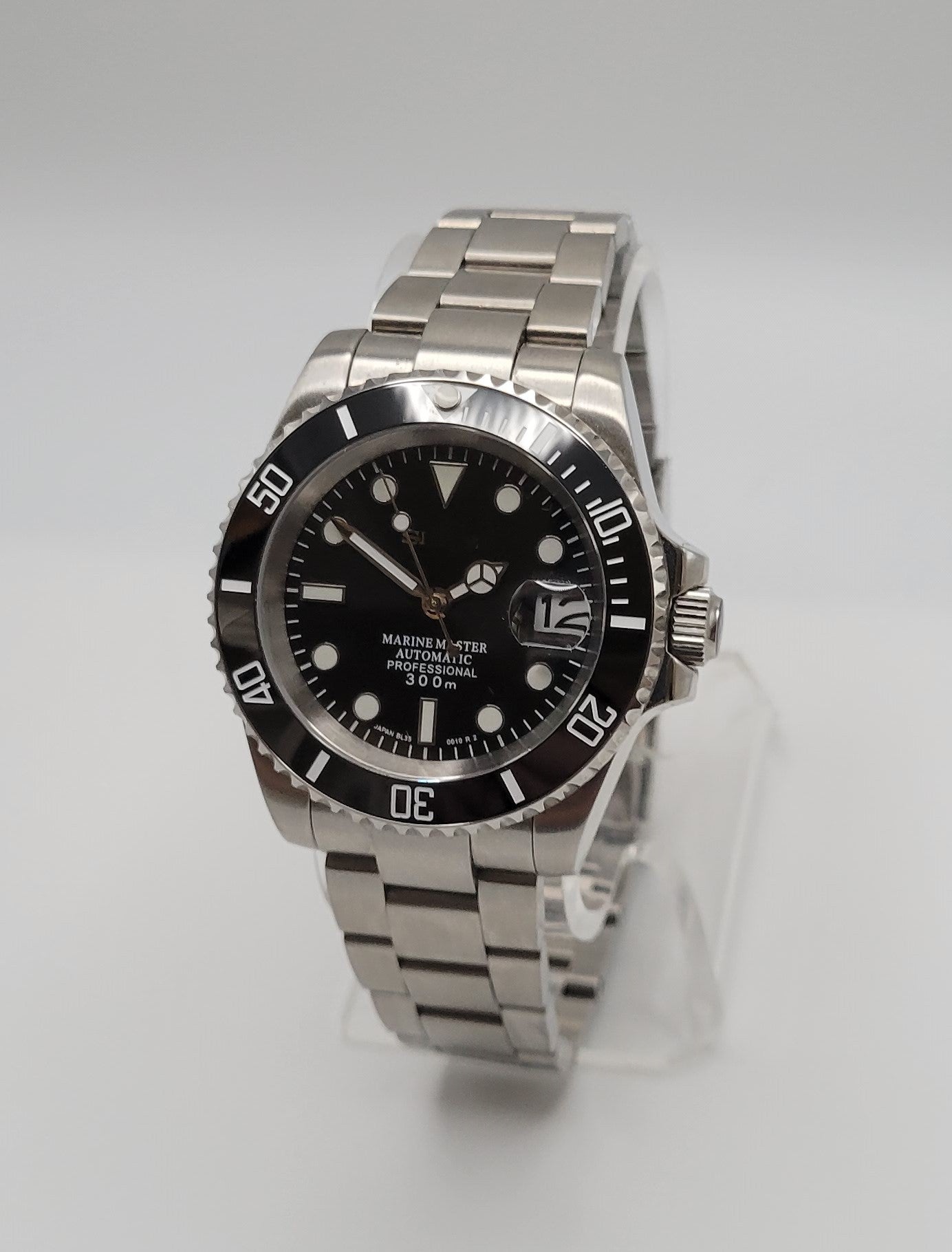 A silver watch with a black bezel and black dial, displayed on a clear stand against a white background.