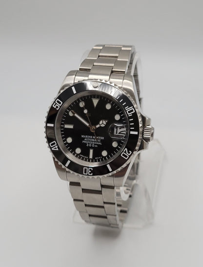 A silver watch with a black bezel and black dial, displayed on a clear stand against a white background.