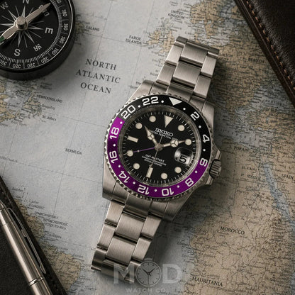 Silver Seiko watch with a black and purple bezel on a world map background