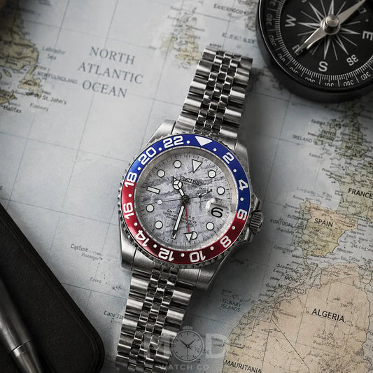 Silver watch with red and blue bezel on a map