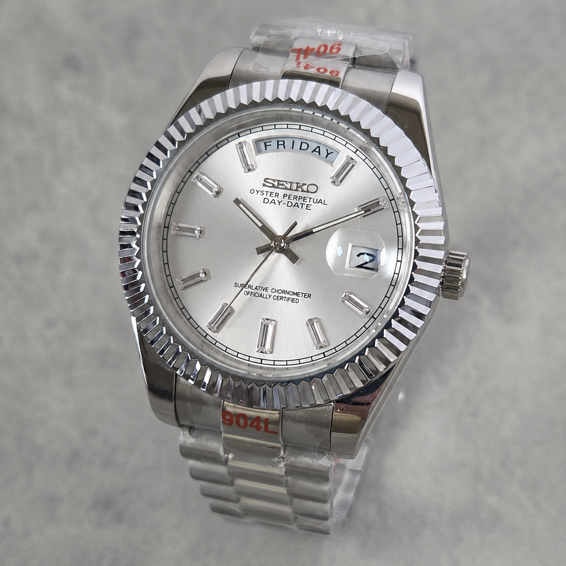 A Seiko Day-Specific wristwatch with a silver-tone stainless steel fluted bezel, silver dial, and matching steel link bracelet, shown on a light gray textured background.