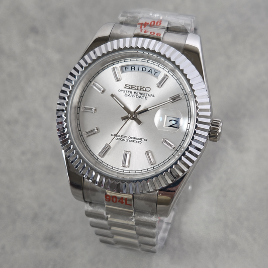 A Seiko Day-Specific wristwatch with a silver-tone stainless steel fluted bezel, silver dial, and matching steel link bracelet, shown on a light gray textured background.