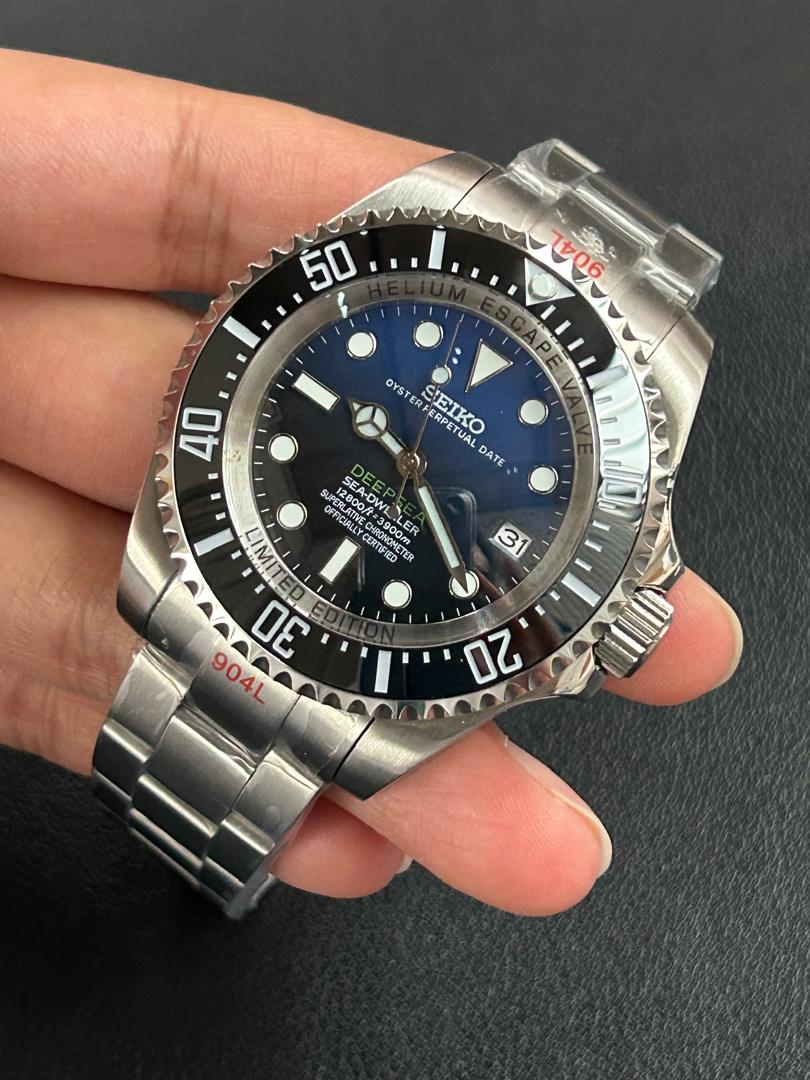 Silver watch with blue dial held in a hand against a dark background